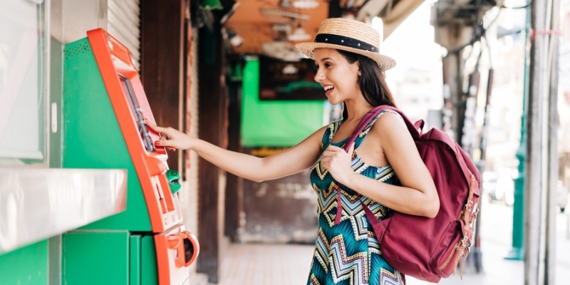 A woman wearing a hat and dress is at an ATM, highlighting the importance of being cautious while using these machines.