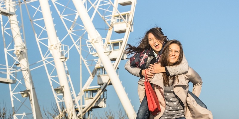 Two friends pose happily in front of a Ferris wheel, enjoying a fun day out in Chicago's lively amusement scene.