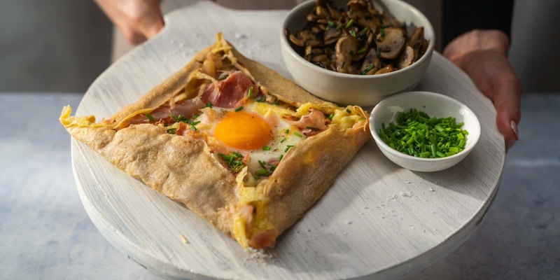 Close-up of a person presenting a plate with a buckwheat galette breakfast sandwich.