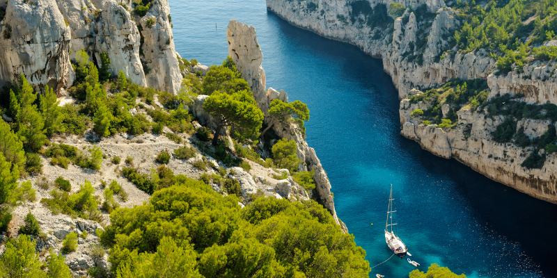 A serene view of a boat anchored in the vibrant blue waters of Calanque d'En-Vau, surrounded by majestic cliffs.