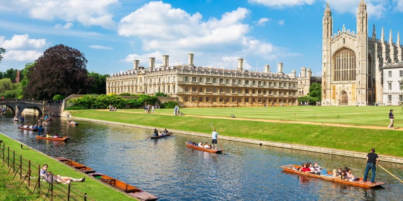 A picturesque scene of individuals in boats on the river, with the grand architecture of Cambridge University visible behind.