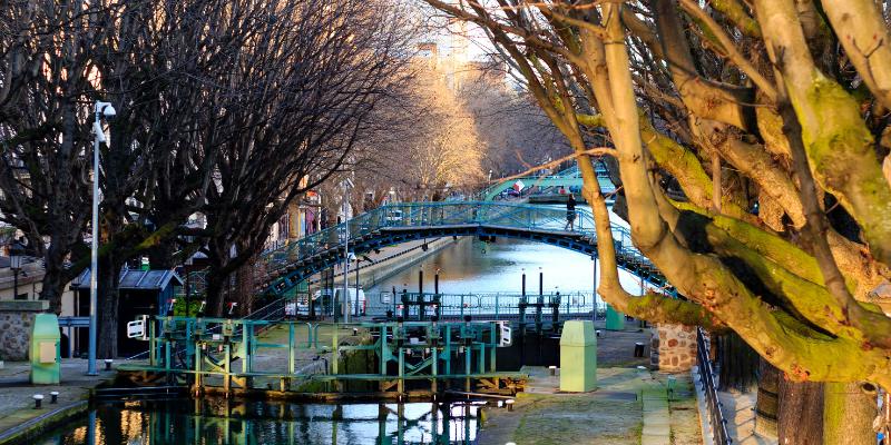 Canal Saint-Martin with a picturesque bridge and vibrant trees flanking the tranquil waters on either side.