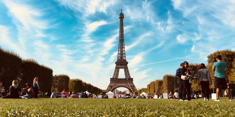 The Eiffel Tower rises majestically above Champ de Mars Park, framed by lush greenery and a vibrant Parisian atmosphere.