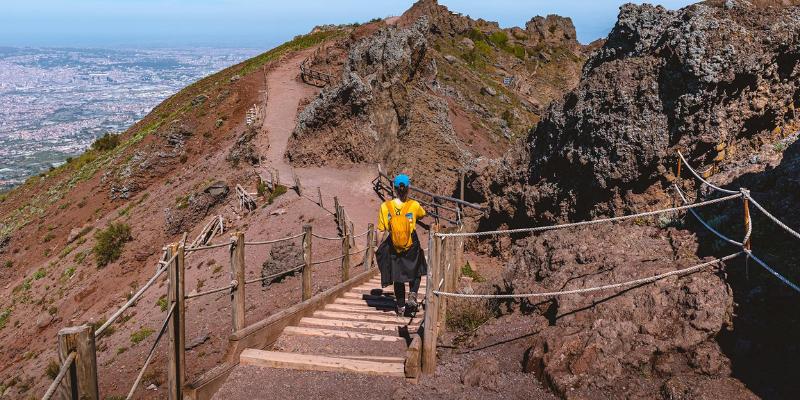 A man climbs the stairs of Mount Vesuvius, navigating the steep path amidst stunning natural scenery.