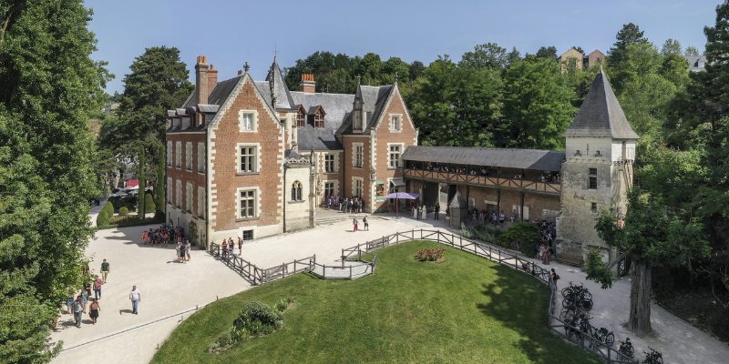 Clos Lucé castle nestled among trees, with people exploring the beautiful grounds and enjoying the scenery.