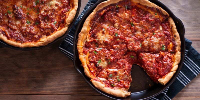 Two deep-dish pizzas sit on a table, one slice removed, emphasizing their rich toppings and crust.