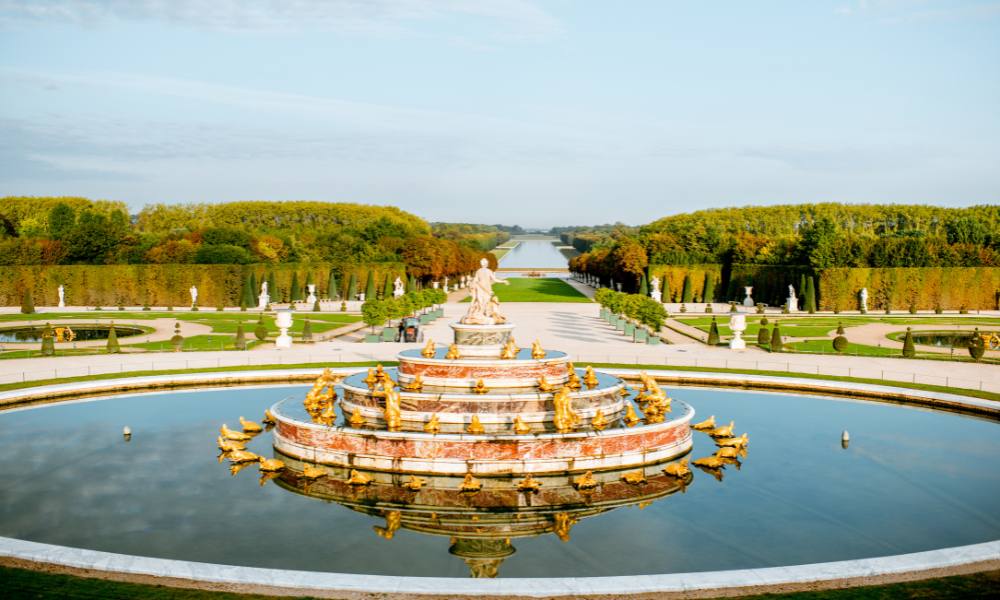 A grand fountain surrounded by lush green lawn at the Palace of Versailles, a top attraction in France.