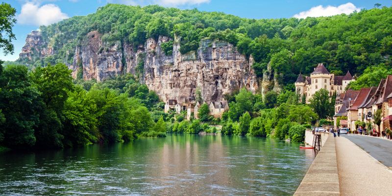 The serene Dordogne River winds through a charming town, dominated by a historic castle overlooking the landscape.