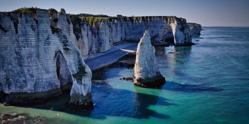 Majestic Étretat Cliffs rise above the Normandy coastline, featuring striking white chalk formations against the blue sea.