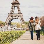 Two women leisurely walk in front of the Eiffel Tower, embodying the charm and beauty of Parisian life.