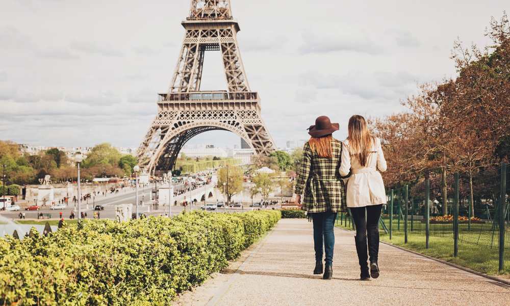 Two women leisurely walk in front of the Eiffel Tower, embodying the charm and beauty of Parisian life.