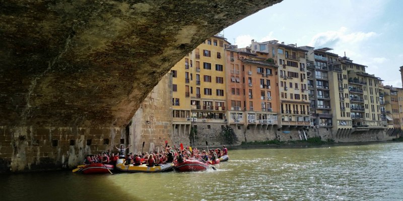 Rafting enthusiasts glide through the Arno River under a beautiful archway in Florence, enjoying the scenic views.