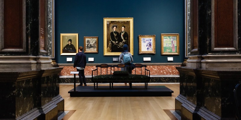 Visitors explore the Fitzwilliam Museum, with a man and woman engaged in viewing the displayed paintings.