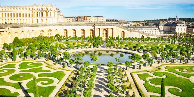 A view of the Palace of Versailles, highlighting its opulent design and the expansive Gardens of Versailles surrounding it.