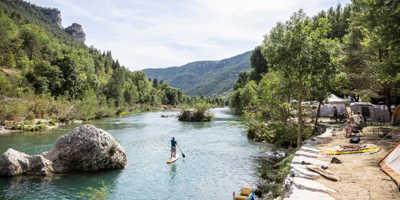 A man paddles a canoe down the scenic Gorges du Tarn river in France, surrounded by stunning natural landscapes.