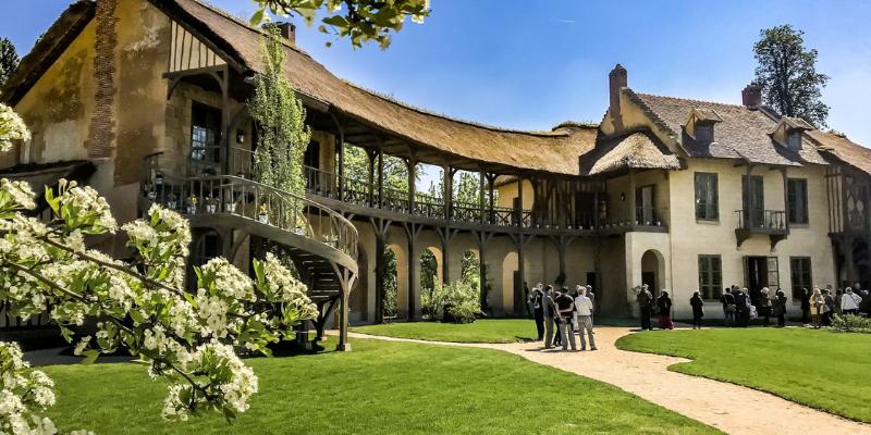 Tourists explore the Duc de la Rochefoucauld's house at Hameau de la Reine, surrounded by lush gardens.