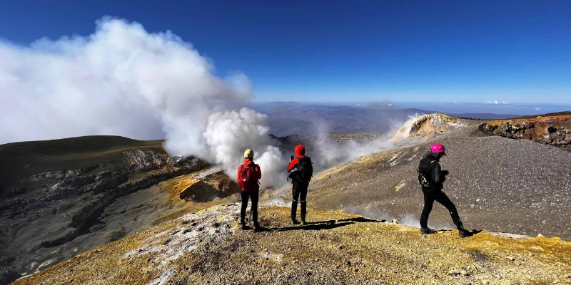 A trio of hikers on Mount Etna, overlooking a dramatic steamy plume from the active volcano.