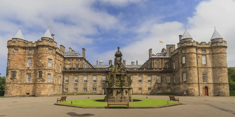 Holyrood Palace stands majestically, featuring an expansive design with a stunning fountain situated at its entrance.