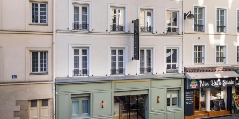 Hôtel La Canopée’s classic facade with a vertical "Hotel" sign by a salad shop.