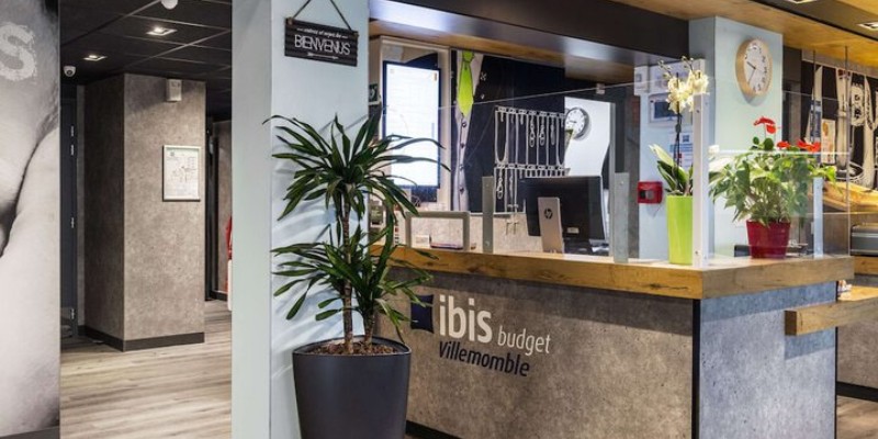 Ibis Budget Villemomble’s modern reception with plants, clock, and protective screen.