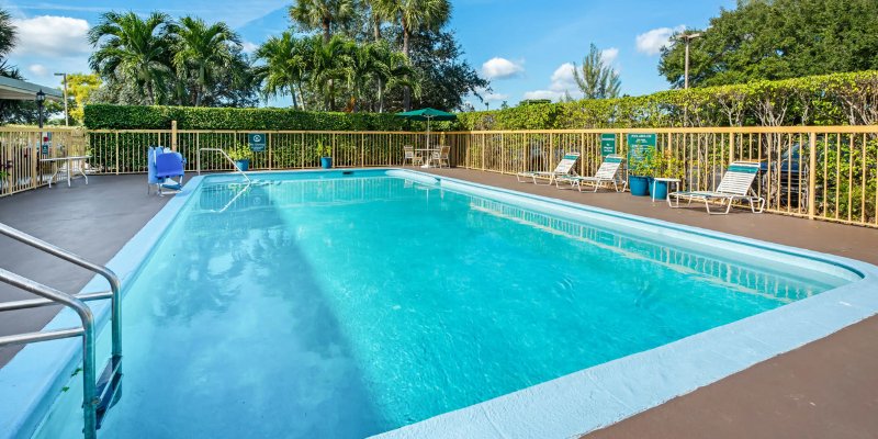 Pool area at La Quinta Inn by Wyndham West Palm Beach, features lounge chairs and palm trees under a clear blue sky.