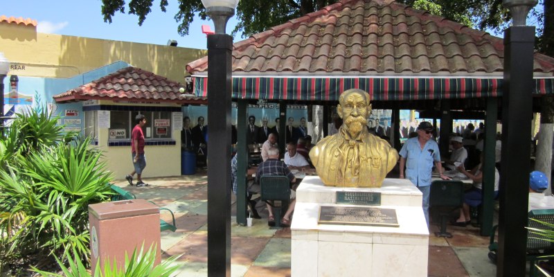 In Little Havana, a statue of a man is featured in a gazebo, with patrons enjoying their time at nearby tables.