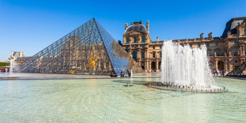 A view of the Louvre Museum in Paris, featuring the famous glass pyramid and elegant classical buildings.