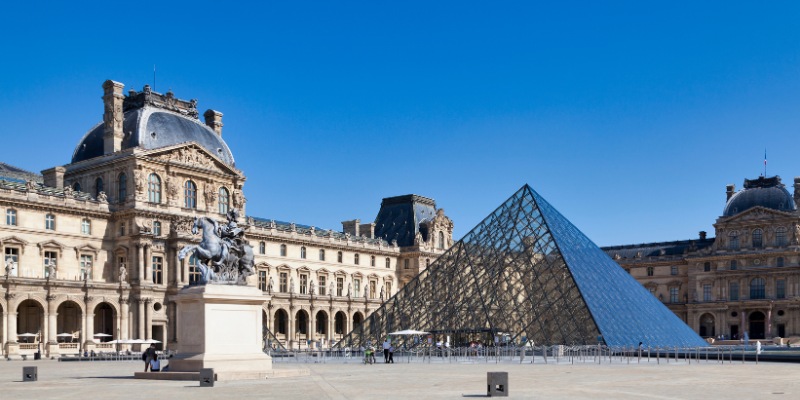 A view of the Louvre Museum in Paris, France, featuring the famous glass pyramid and grand historic facade.