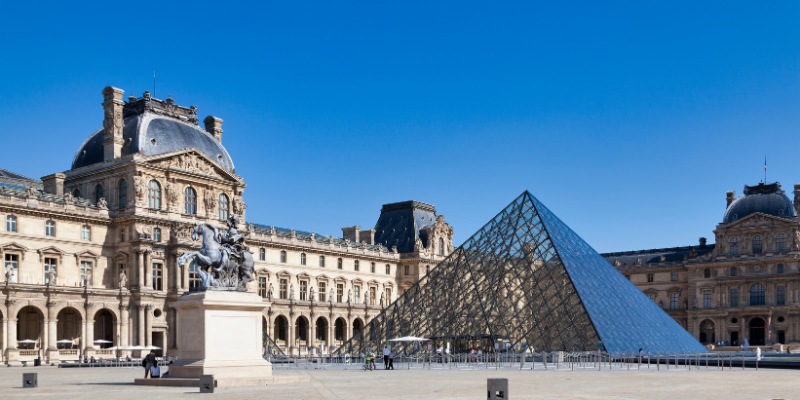 A view of the Louvre Museum in Paris, France, featuring its famous glass pyramid and grand facade.