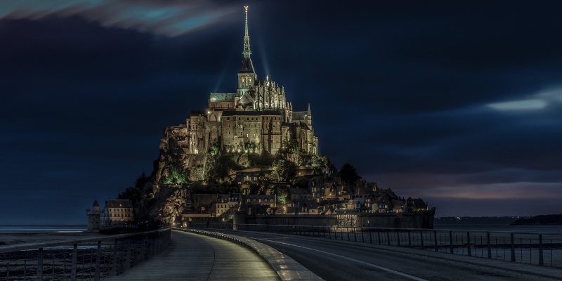 Mont Saint Michel at night, showcasing its illuminated silhouette rising majestically from the waters of Normandy, France.