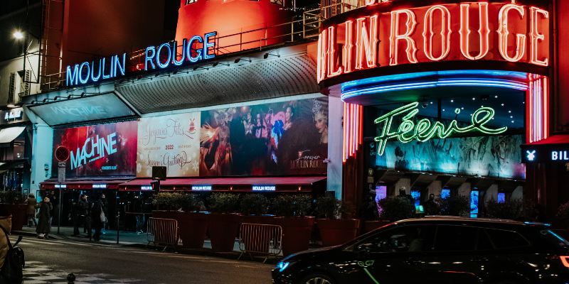 A lively city street at night with bright neon signs and cars reflecting the energetic spirit of Moulin Rouge.