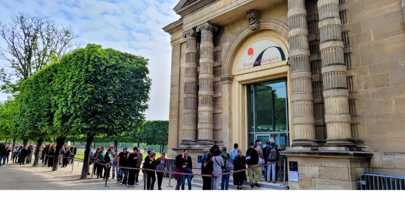 Visitors line up outside the Musée de l'Orangerie, framed by vibrant trees in a picturesque setting.