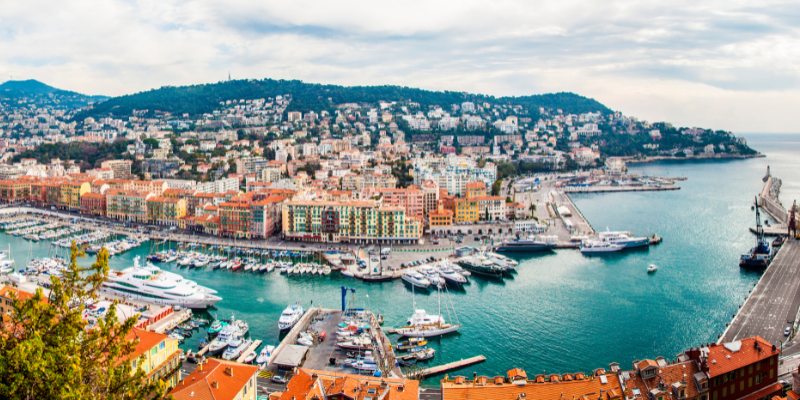 Scenic harbor in Nice, France, showcasing boats moored alongside charming buildings and the Mediterranean coastline.