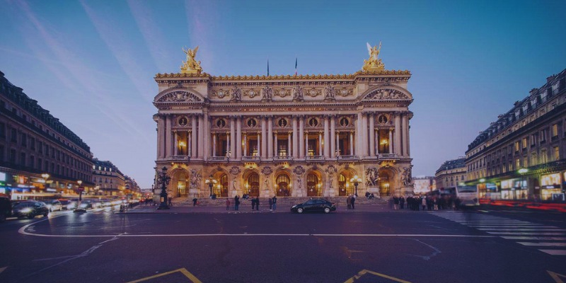 Dusk settles over the Palais Garnier, Paris, highlighting its ornate façade and majestic presence in the evening light.