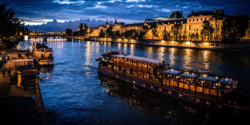 A charming dinner cruise on the Seine River in Paris, with a boat sailing peacefully at night under twinkling lights.