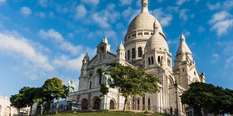 The Sacred Heart Basilica in Paris, France, showcasing its iconic white domes against a clear blue sky.