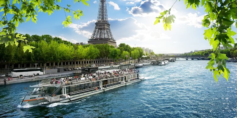 Tourists enjoy a Seine River cruise with a stunning view of the Eiffel Tower in the background.