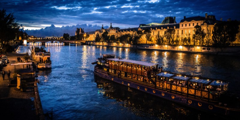 A serene Seine River cruise boat navigates the river at night, surrounded by the tranquil glow of city lights.