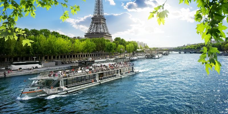 A scenic view of a riverboat navigating the Seine River, with iconic Parisian landmarks in the background.