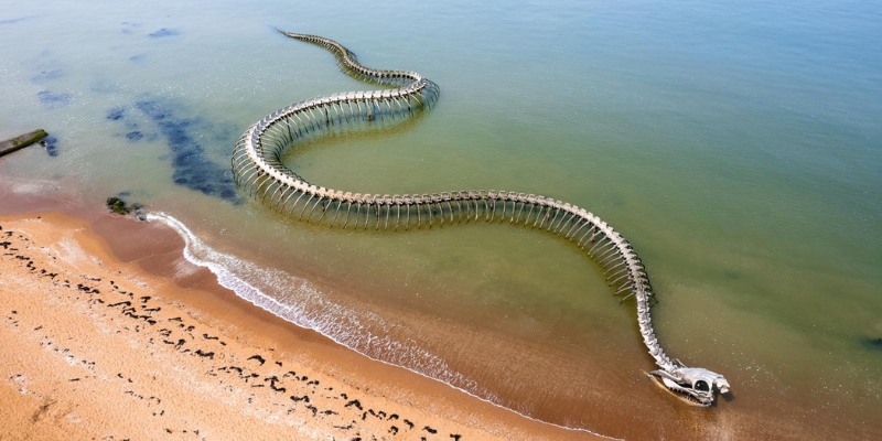 The "Serpent d'océan" sculpture, a long snake, lies on the beach, showcasing a unique fusion of art and coastal scenery.