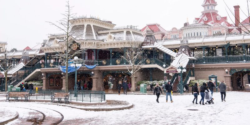 Snow blankets Disneyland Paris, creating a magical winter wonderland scene with iconic attractions in the background.