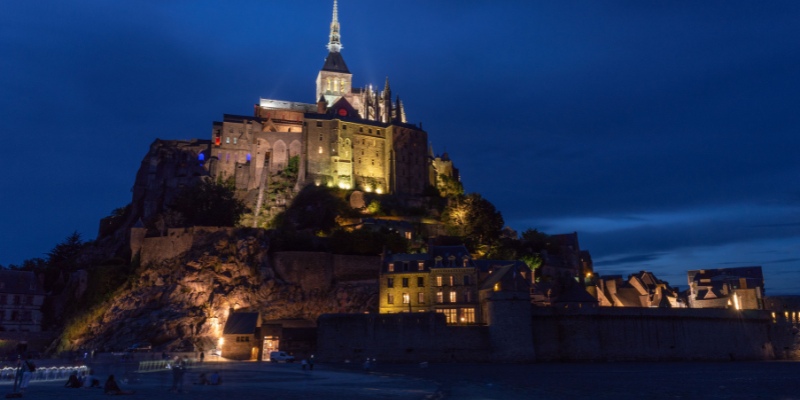 Night view of Mont Saint-Michel, beautifully lit, highlighting its iconic silhouette and surrounding waters.