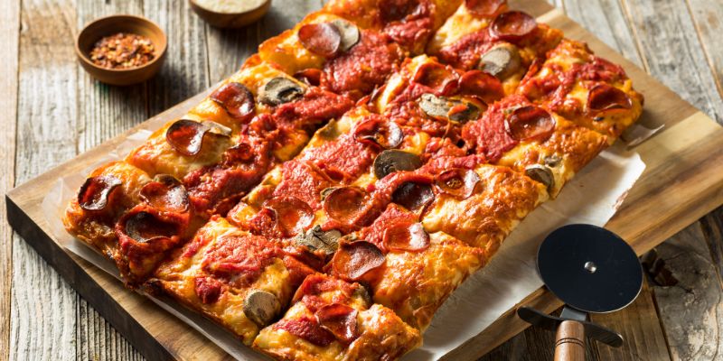 A delicious tavern-style pizza on a cutting board, accompanied by a pizza cutter for easy slicing.