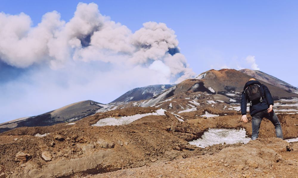 A hiker with a backpack gazes out from a mountain summit, enjoying the expansive view of the landscape below.