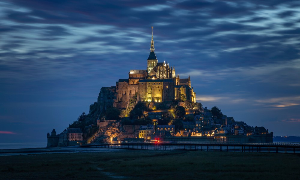 Night view of Mont Saint-Michel, a stunning island commune in Normandy, France, illuminated against a dark sky.