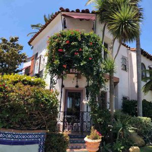 Villa Rosa Inn features a lovely house with a balcony, surrounded by vibrant plants in the front yard.