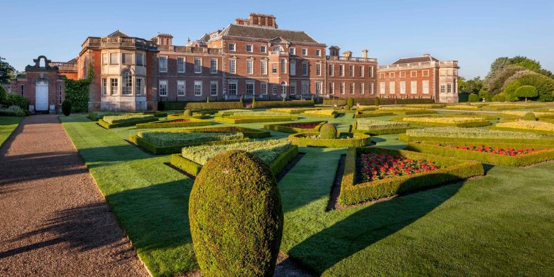 A beautifully manicured formal garden at Hampton Court Palace, showcasing vibrant flowers and elegant pathways.