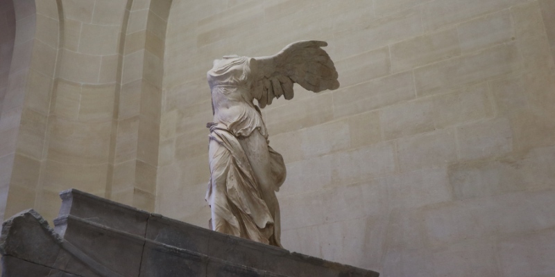 A statue of an angel, resembling the Winged Victory of Samothrace, gracefully sits atop a pedestal.