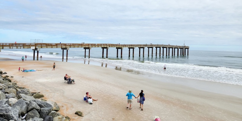 People relax and have fun on the beach near a pier at Anastasia Beach, enjoying the sun and ocean waves.