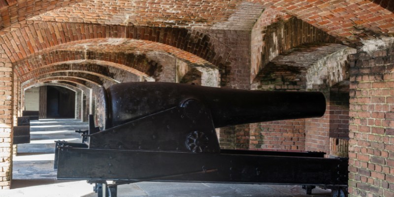 A Civil War cannon positioned inside a tunnel beneath a brick wall, showcasing historical military equipment.